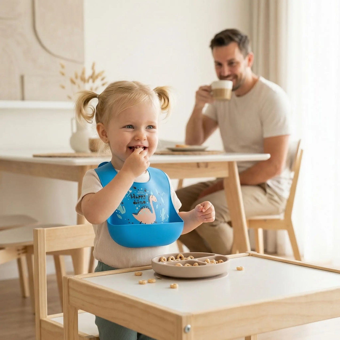 Fillette grignotant des cereales avec son bavoir impermeable silicone bleu motif dinosaure
