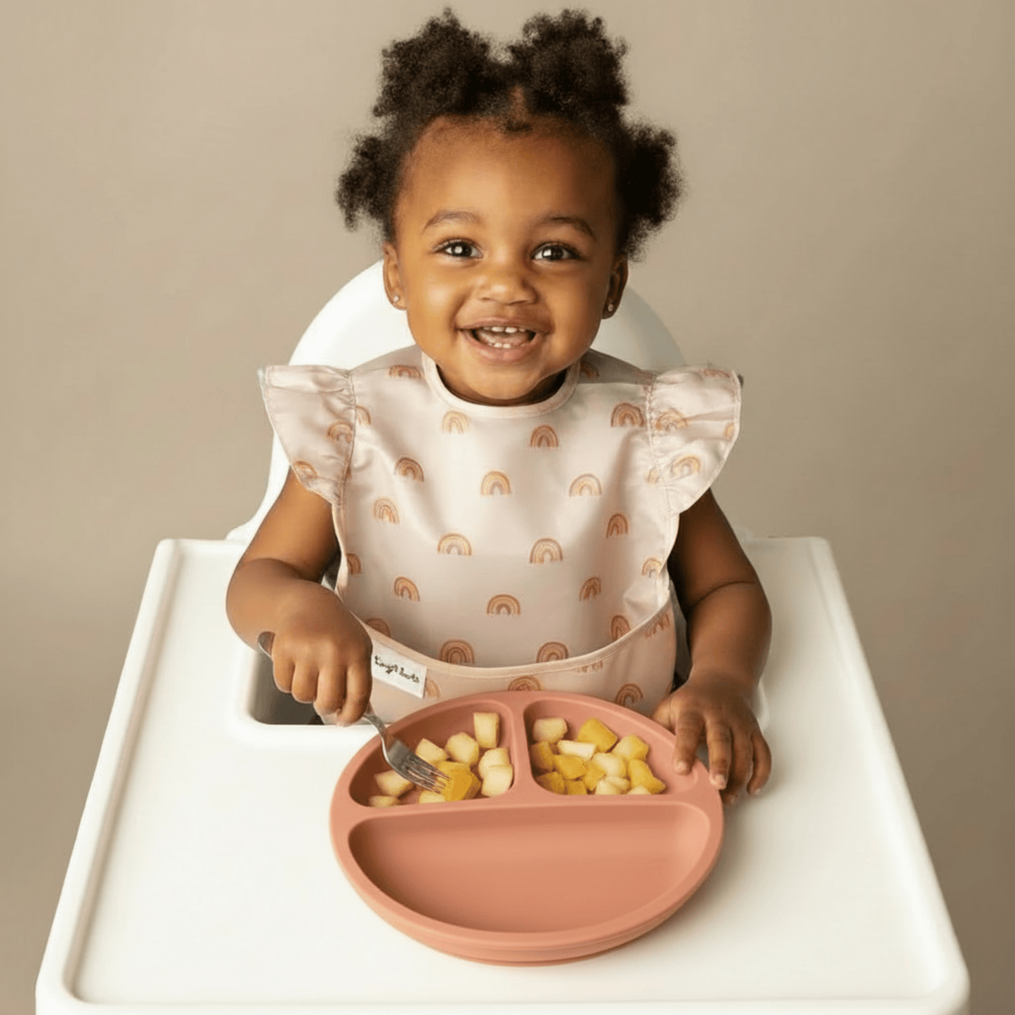 Une petite fille mange des morceaux de fruits avec sa petite fourchette dans son assiette bebe 3 compartiments et ventouses en silicone coloris orange