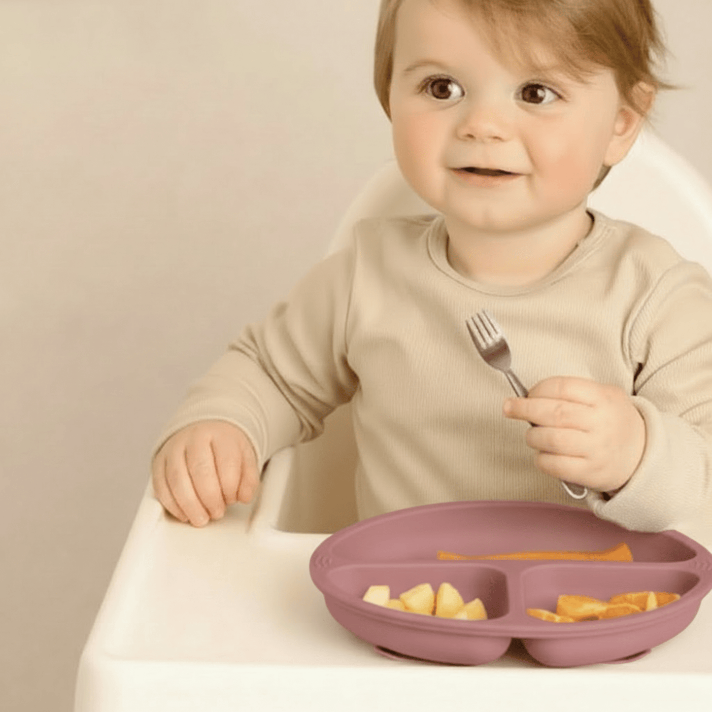 Un enfant prend ses aliments avec sa fourchette inox dans l'assiette bebe silicone  à 3 compartiments et ventouses coloris rose