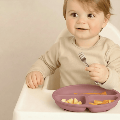 Un enfant prend ses aliments avec sa fourchette inox dans l'assiette bebe silicone  à 3 compartiments et ventouses coloris rose