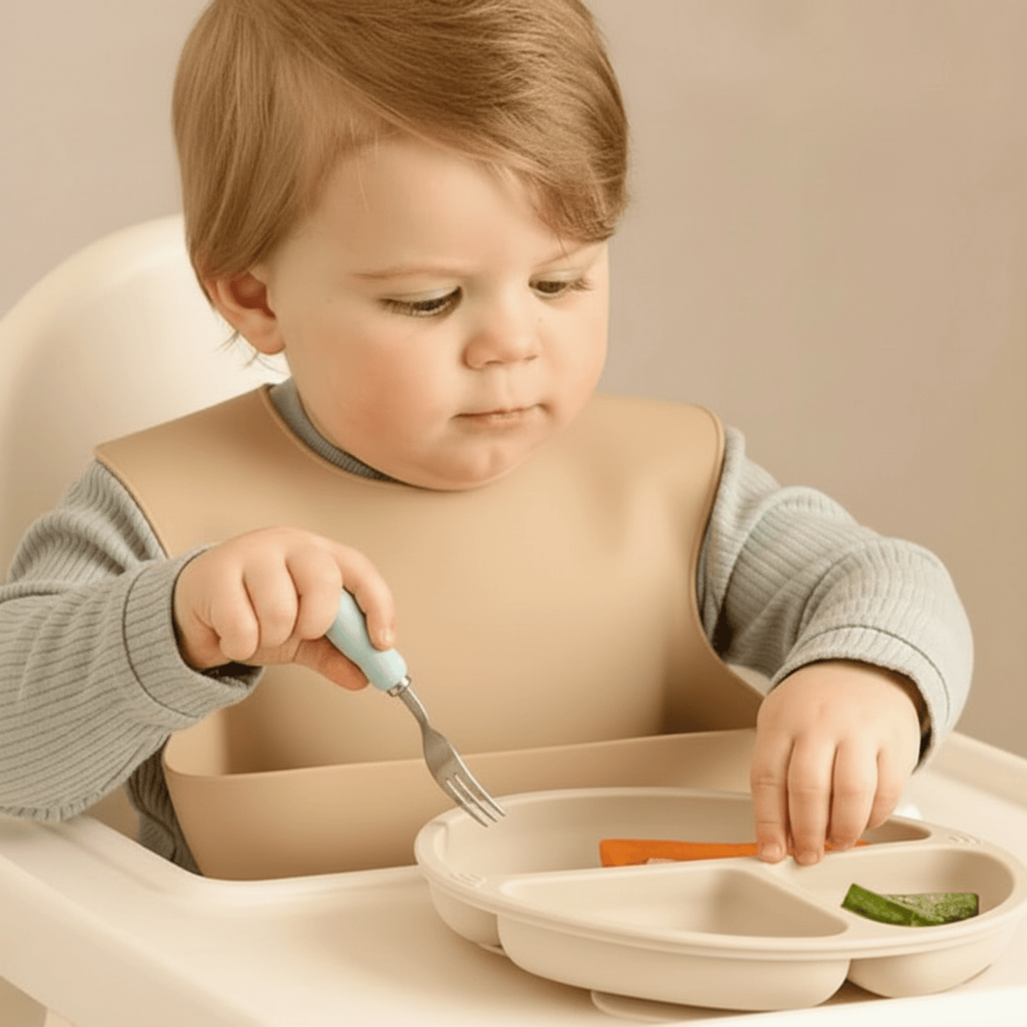 un enfant avec un bavoir silicone récupérateur et sa petite fourchette mange des légumes dans son assiette bebe silicone beige 3 compartiments et ventouses