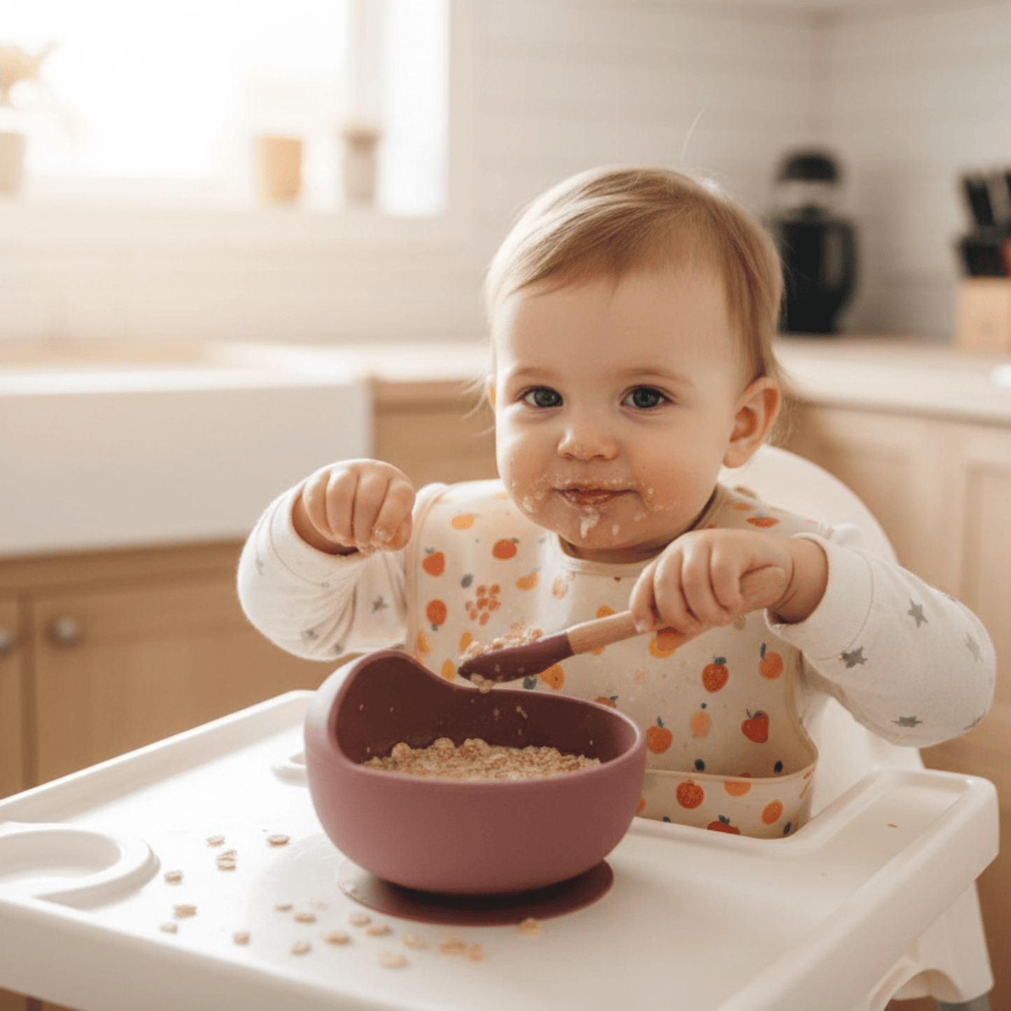 une fillette dans sa chaise haute mange des céréales au lait dans son assiette bebe ventousée coloris cerise avec sa cuillère assortie
