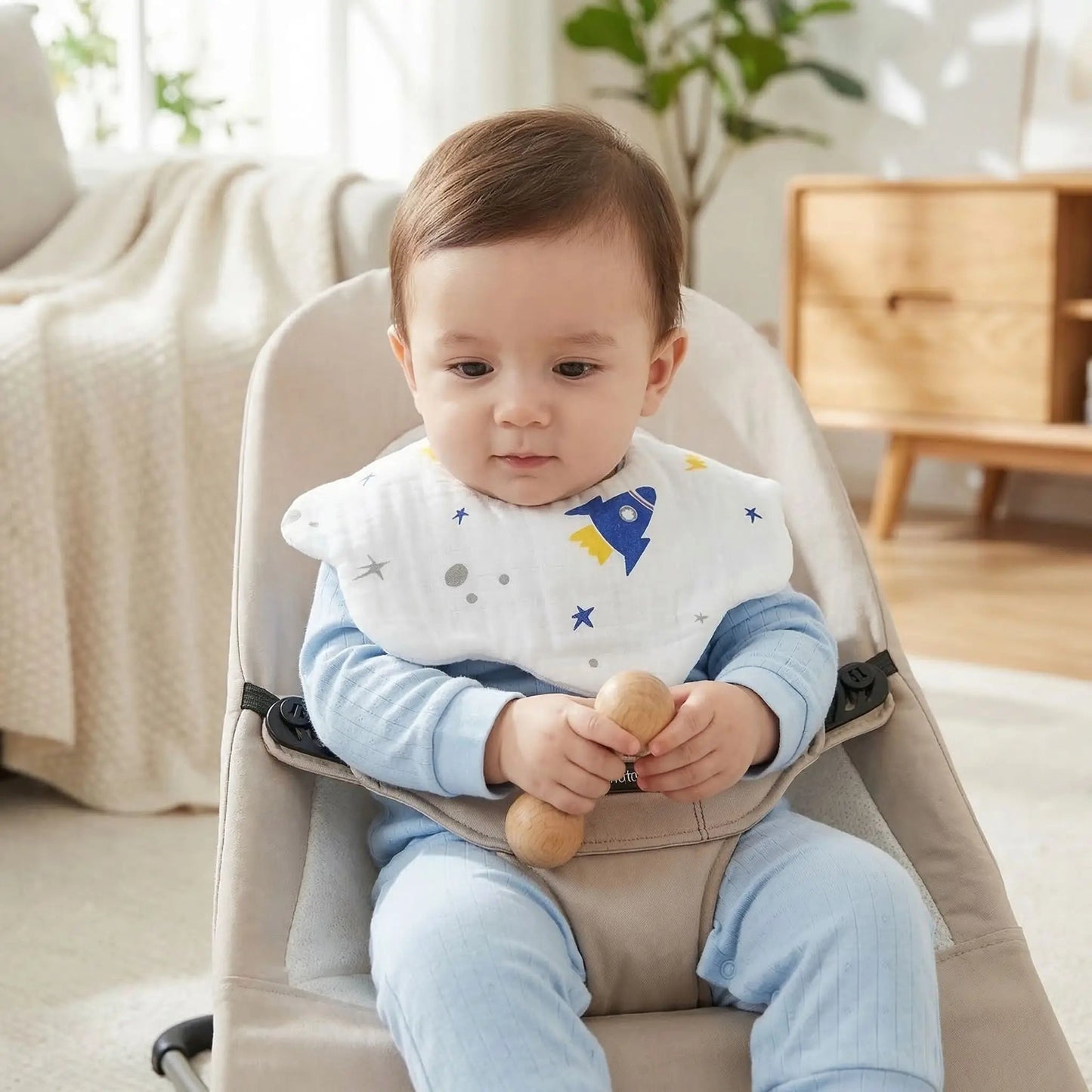 enfant qui joue avec un hochet dans son siège relax et porte le bavoir bebe en coton design fleur motif fusee
