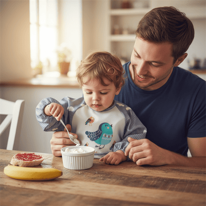 un enfant prend son goûter sur les genoux de son papa en portant le bavoir impermeable gris motif oiseau