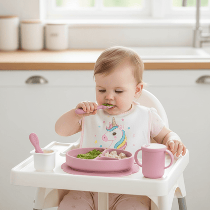 Une fillette utilise son couvert bébé silicone rose pour son repas de manière autonome