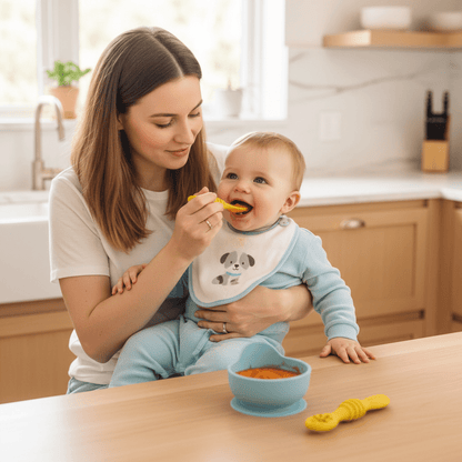 Maman nourrit son bébé avec la cuillère silicone jaune. La cuillère silicone texturée est posée sur table