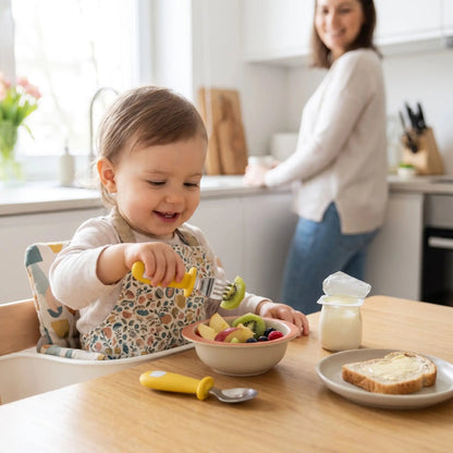 un enfant goûte en piquant des morceaux de fruits avec son couvert pour bebe coloris jaune moutarde