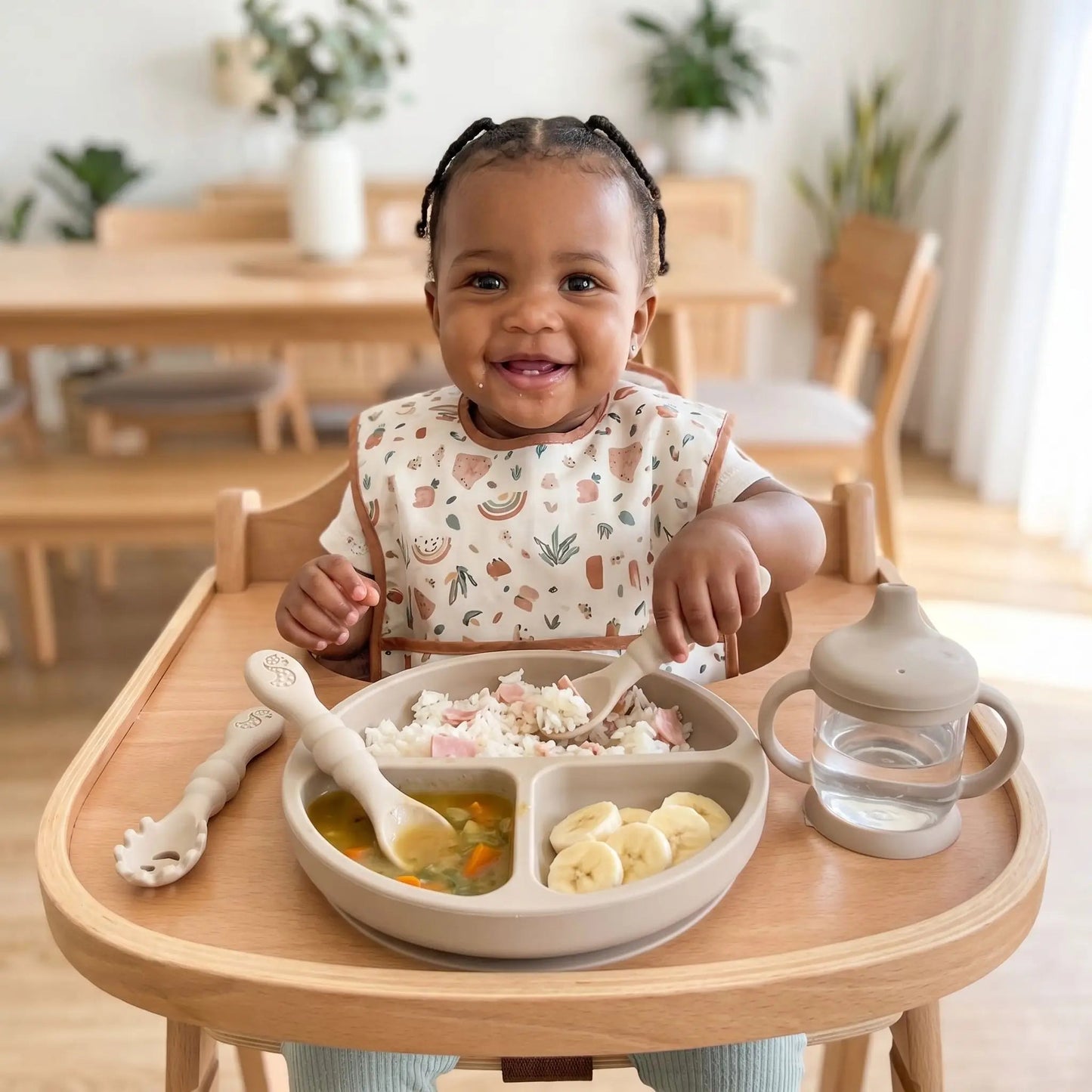 une fillette mange en autonomie son repas dans une assiette compartimentée avec sa cuillere ergonomique bebe coloris beige
