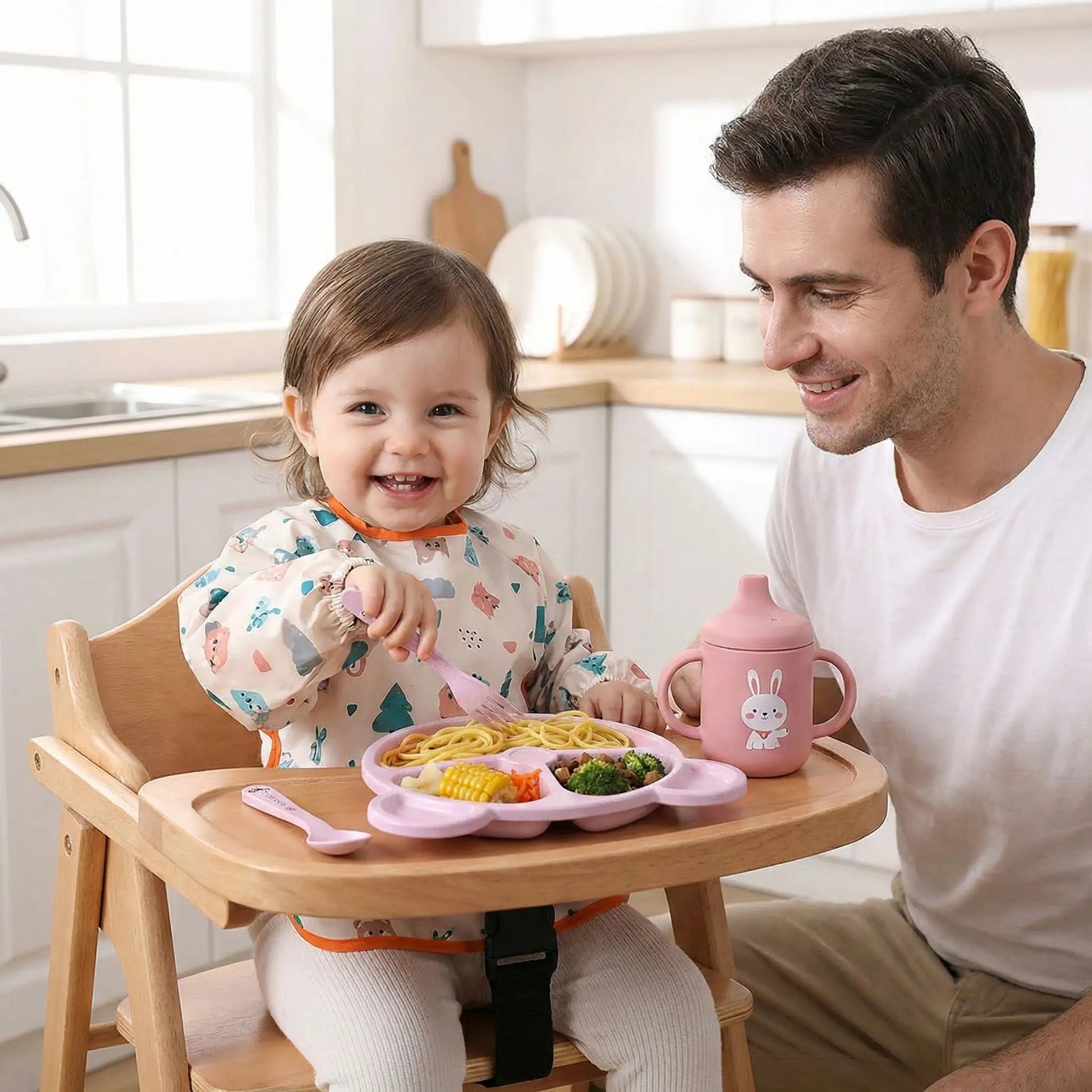 une fillette de 18 mois déguste son repas dans la vaisselle bebe écologique coloris rose. Son père est heureux de constater son plaisir d'utiliser sa propre vaisselle de grande