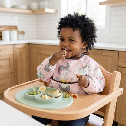 une fillette goûte des fruits et porte le bavoir bébé manche longue impermable motif licornes