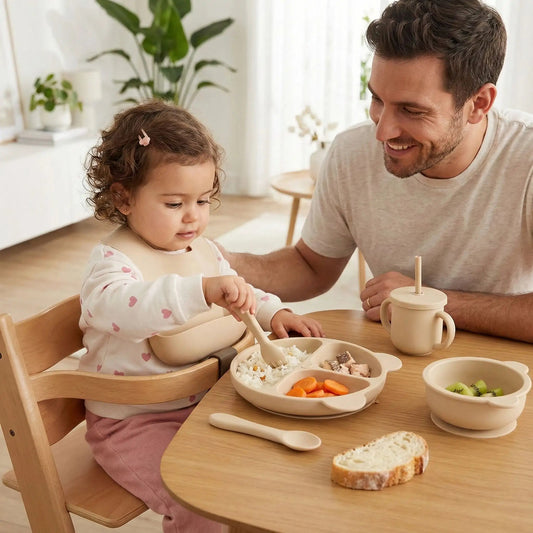 une fillette de 18 mois prend son repas dans le set vaisselle bébé complet beige. Son père est fier de la voir se débrouiller comme une grande.