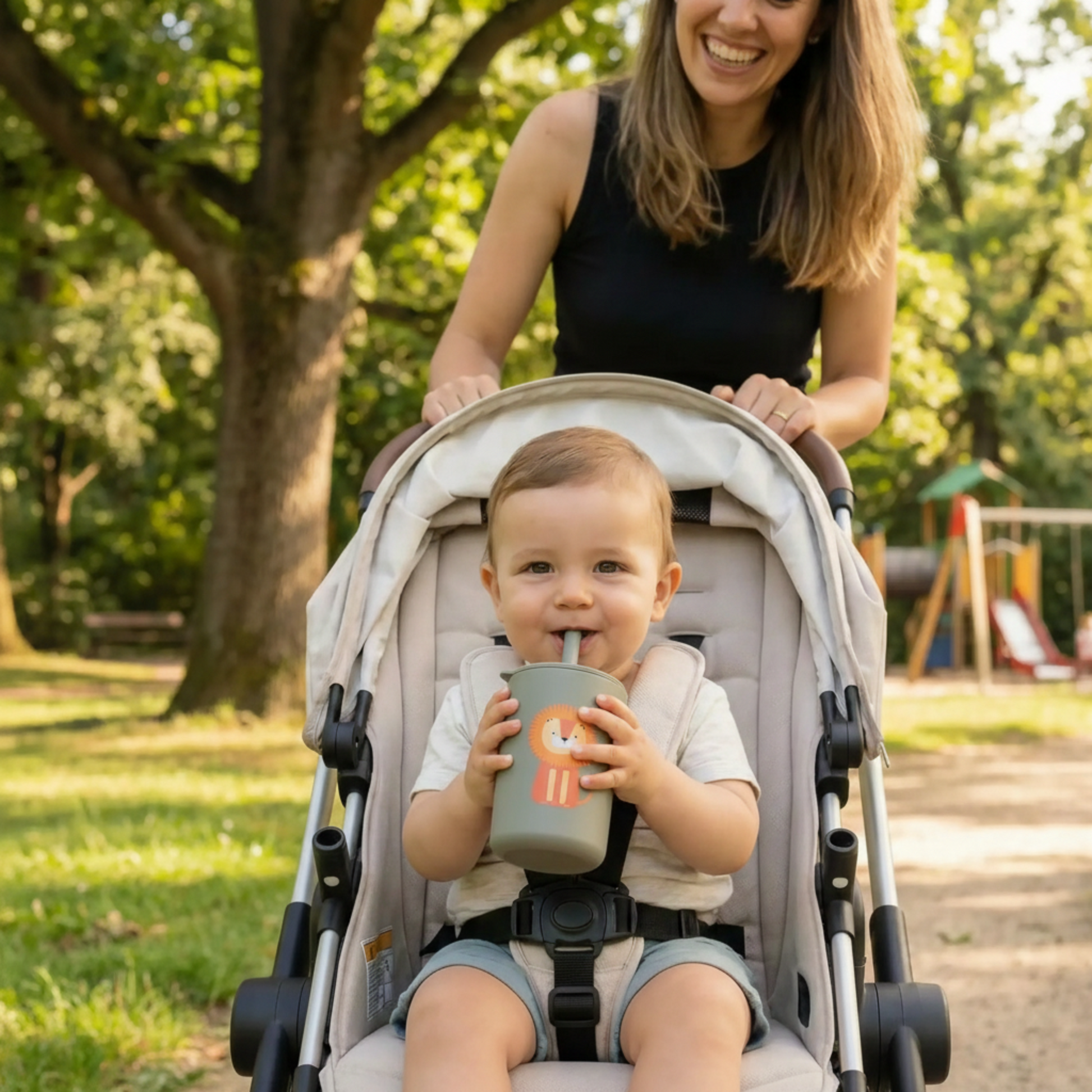 Bébé de 8 mois se promenant en poussette dans un parc. Son verre avec paille en silicone coloris gris lion est parfaitement adapté à ses petites mains