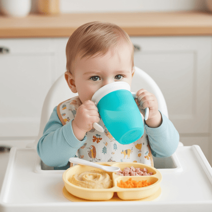repas d'un enfant dans sa chaise haute avec son assiette compartimentée contenant purée, jambon et carottes râpées et tenant sa tasse d'apprentissage 360 coloris bleu