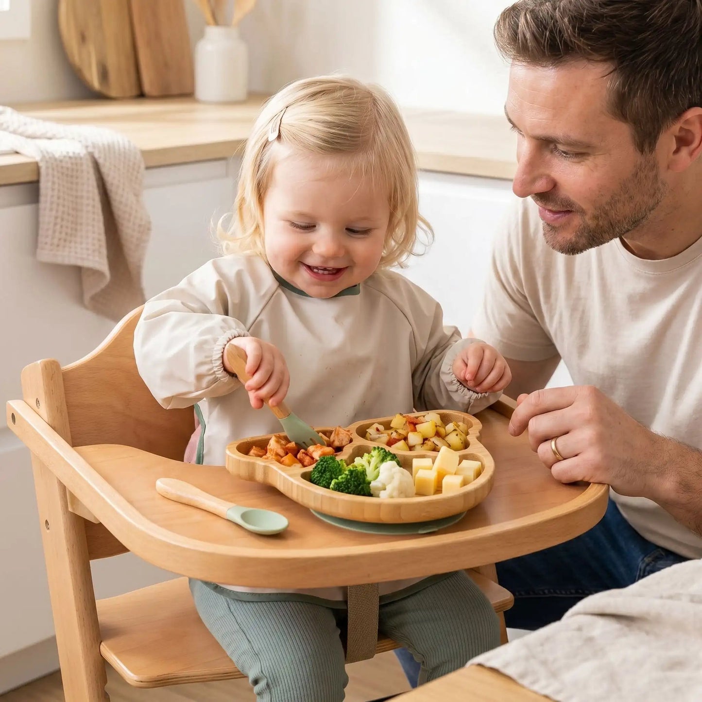 une fillette encouragée par son père pique des morceaux de viande dans l'assiette compartimentée en bambou avec la fourchette du set de vaisselle pour bebe coloris vert