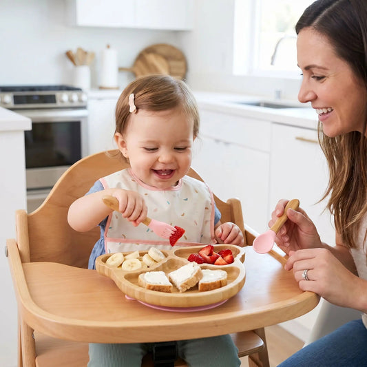 c'est le goter avec maman. La fillette utilise la fourchette du set de vaisselle pour bebe coloris rose pour piquer un morceau de fraise. L'assiette 3 compartiments en bambou est garnie de fruits et de tartines de fromage frais. 