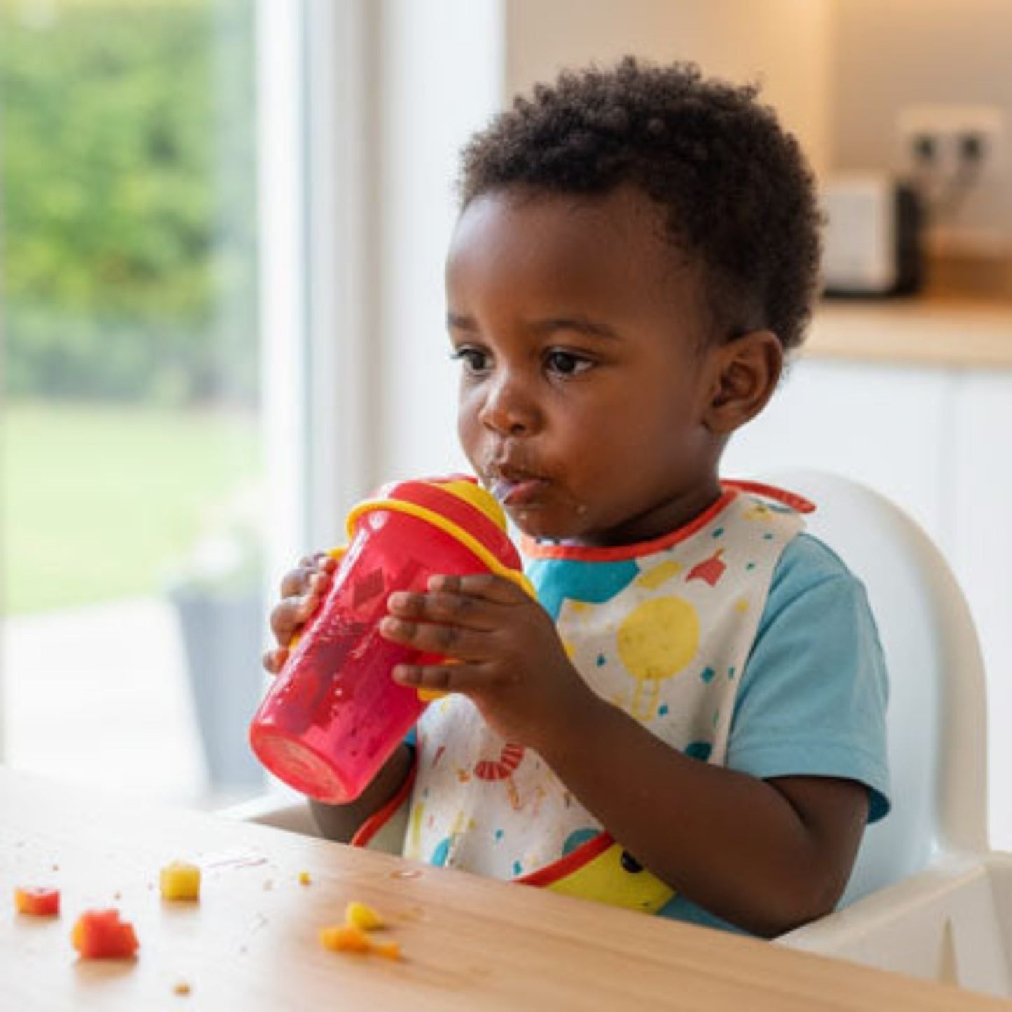 un enfant mangeant des fruits dans sa chaise haute boit dans son verre bebe gourde rouge