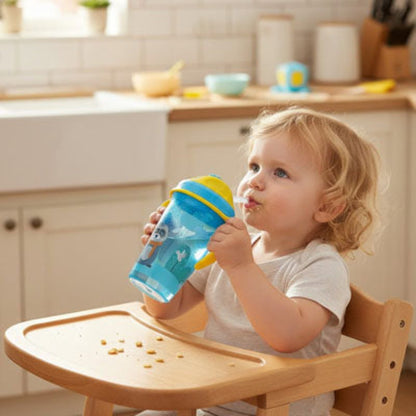 Fillette dans sa chaise haute buvant de façon autonome dans son verre bebe gourde bleu en fin de goûter 