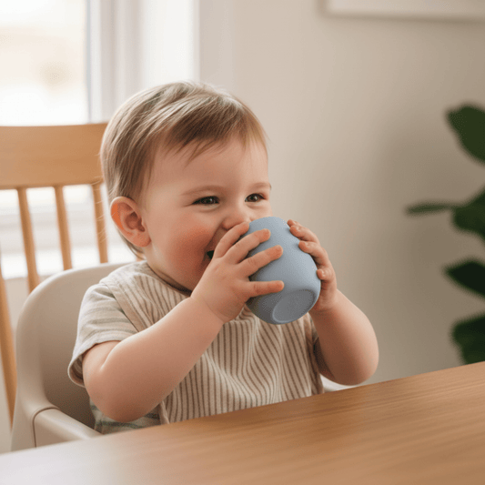 enfant à table dans son réhausseur de chaise tenant seul son mini verre bebe en silicone coloris bleu