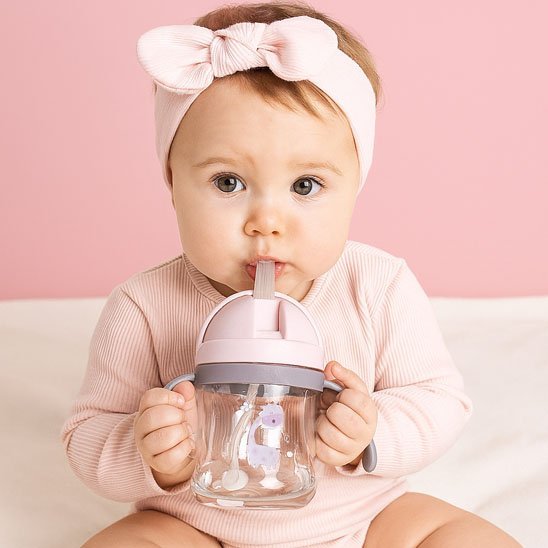 un fillette tient son verre bébé avec paille rose et fait l'apprentissage de l'aspiration